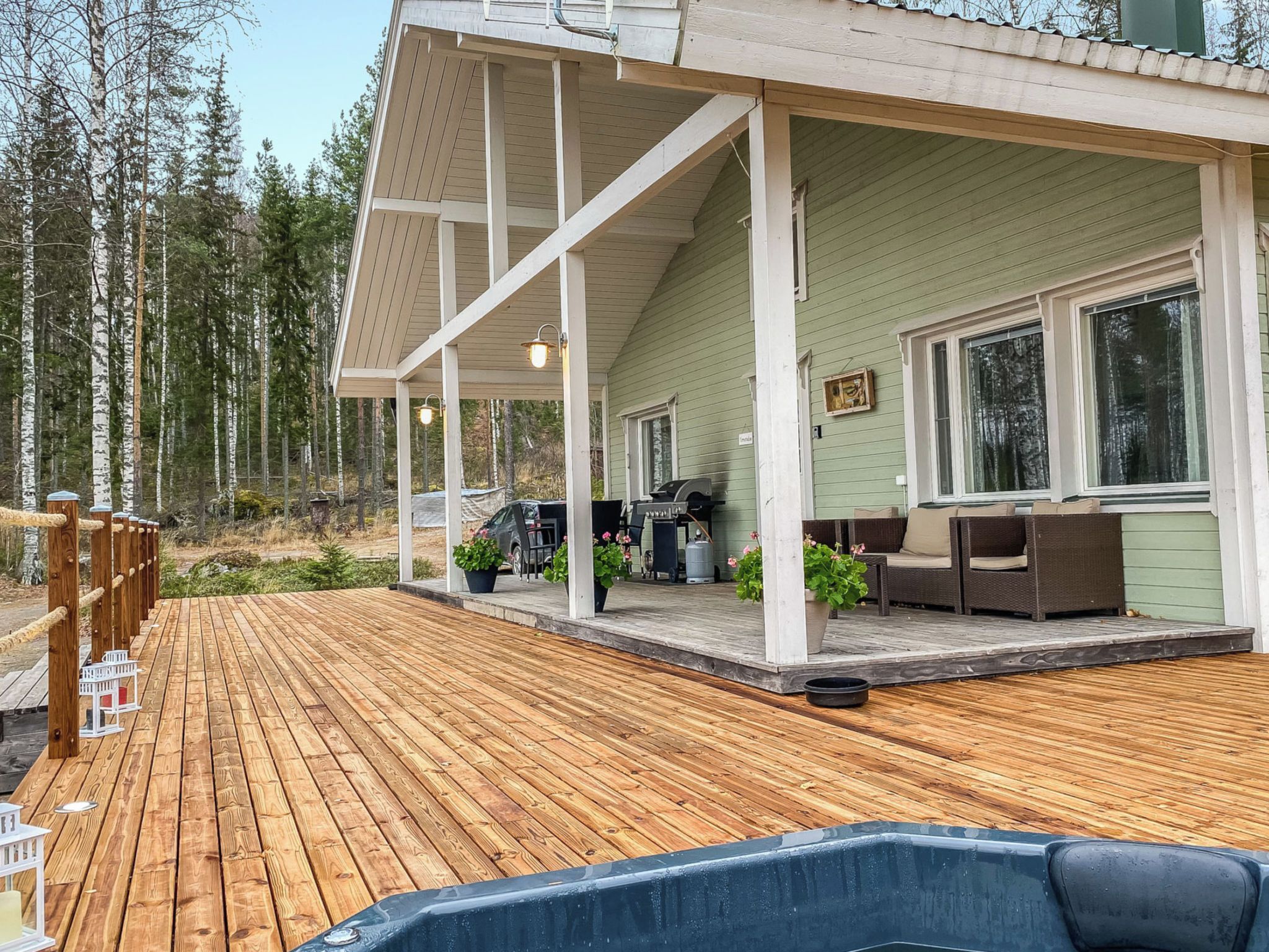 Eine Holzterrasse mit Whirlpool, Gartenmöbeln und einer überdachten Veranda.
