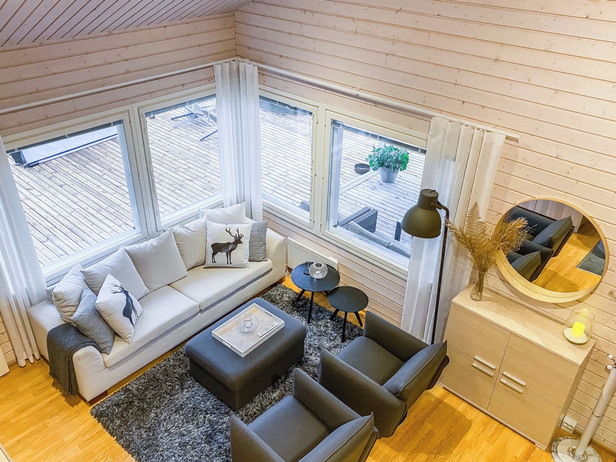 Ein modernes Wohnzimmer mit einer Couch, zwei Sesseln, einem Couchtisch und einem Beistelltisch. Drei Fenster sorgen für natürliches Licht und bieten einen Blick ins Freie.