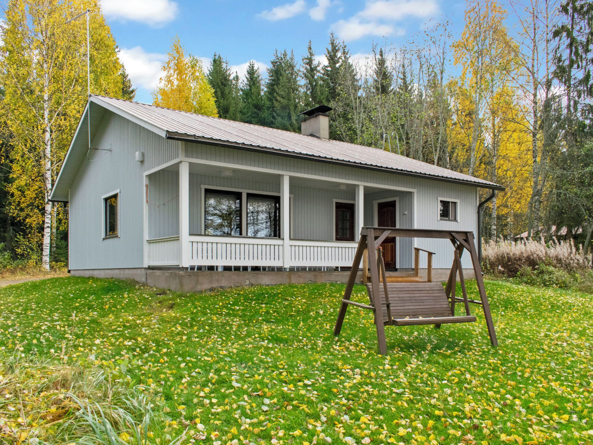 Ein Bungalow mit Veranda, umgeben von einem Rasen und Bäumen.