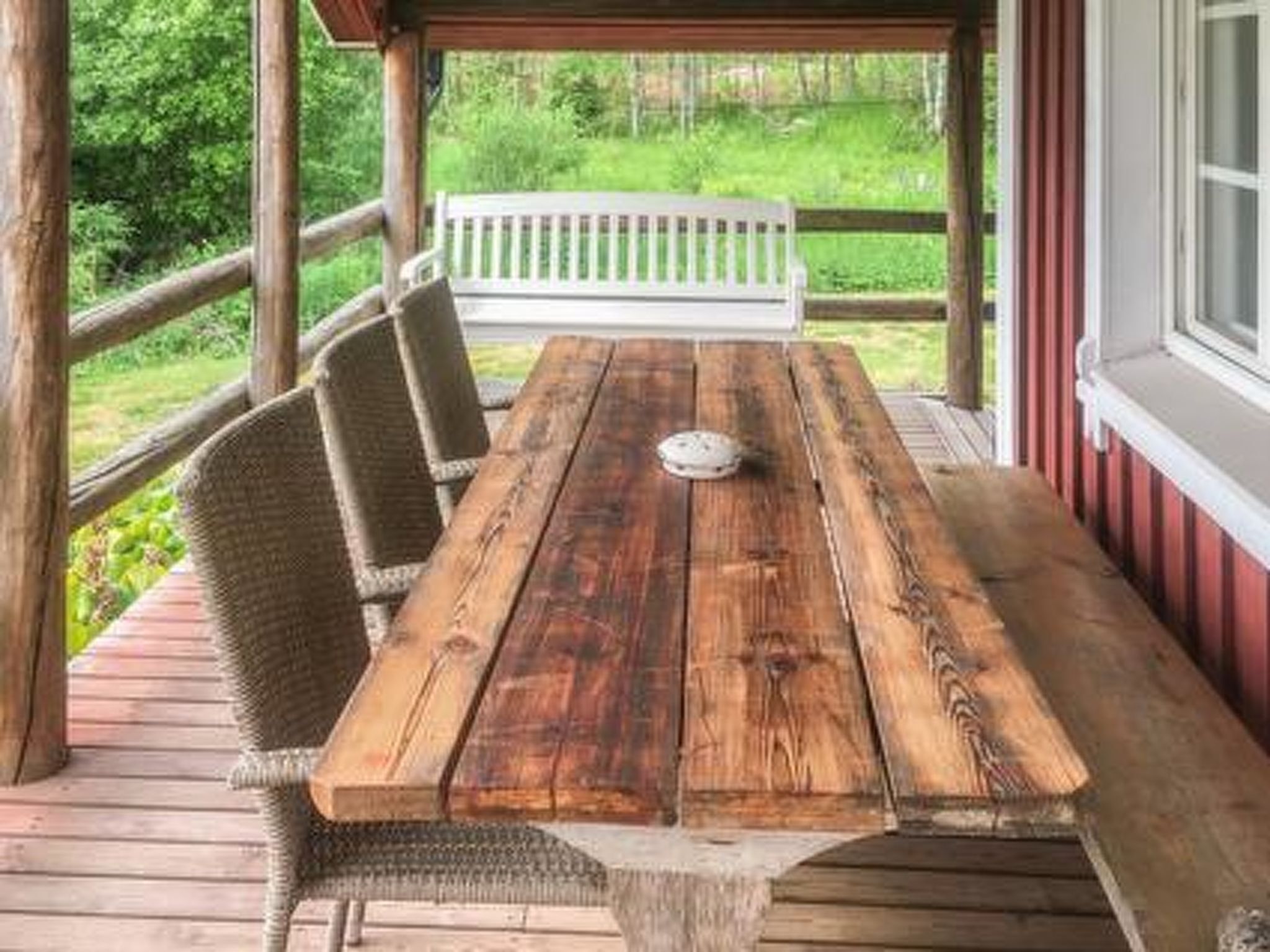 Eine Holzterrasse mit Tisch und Stühlen, eine weiße Bank und Blick ins Grün.