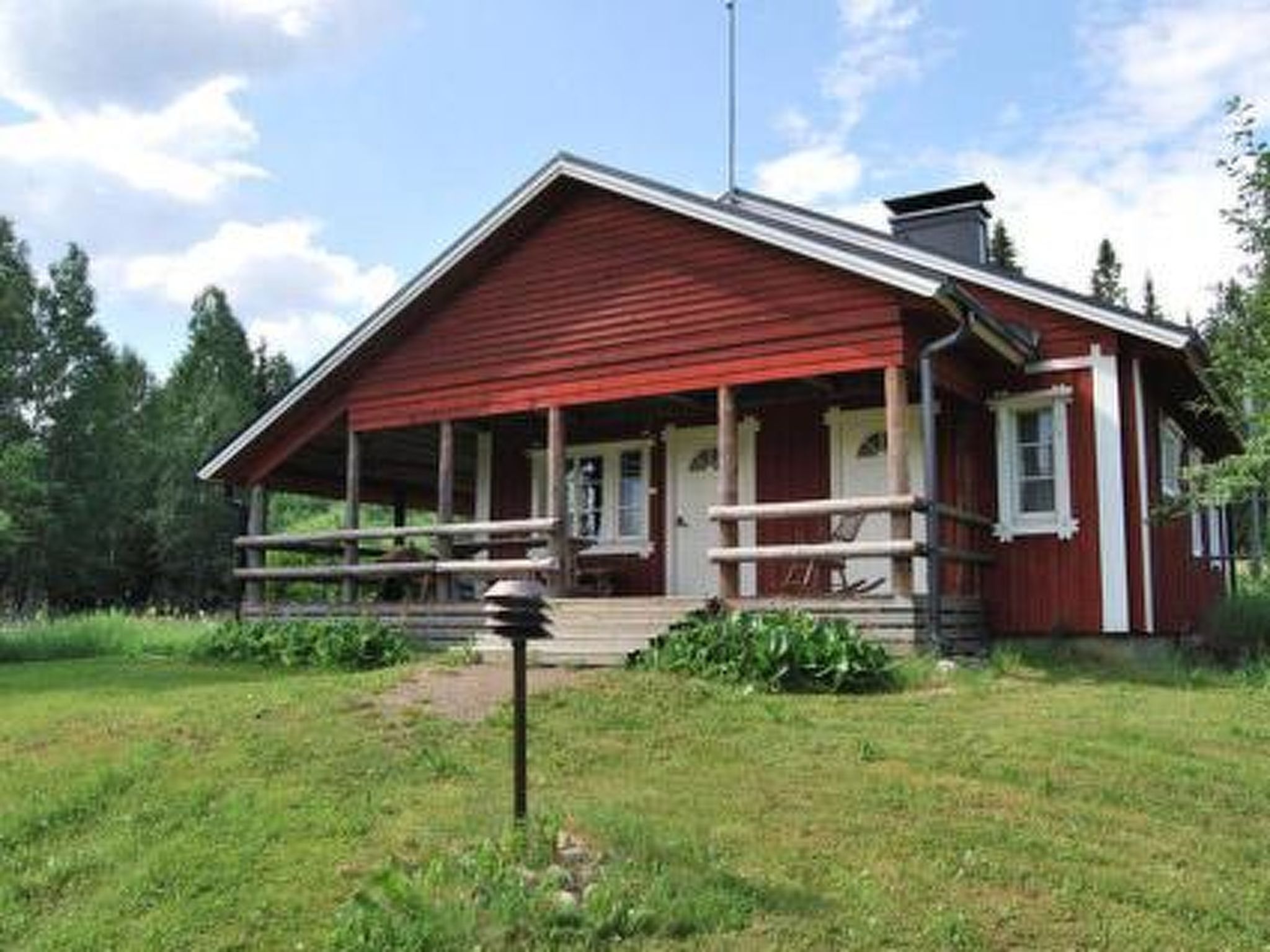 Eine rote Holzhütte mit Veranda, umgeben von viel Grün.