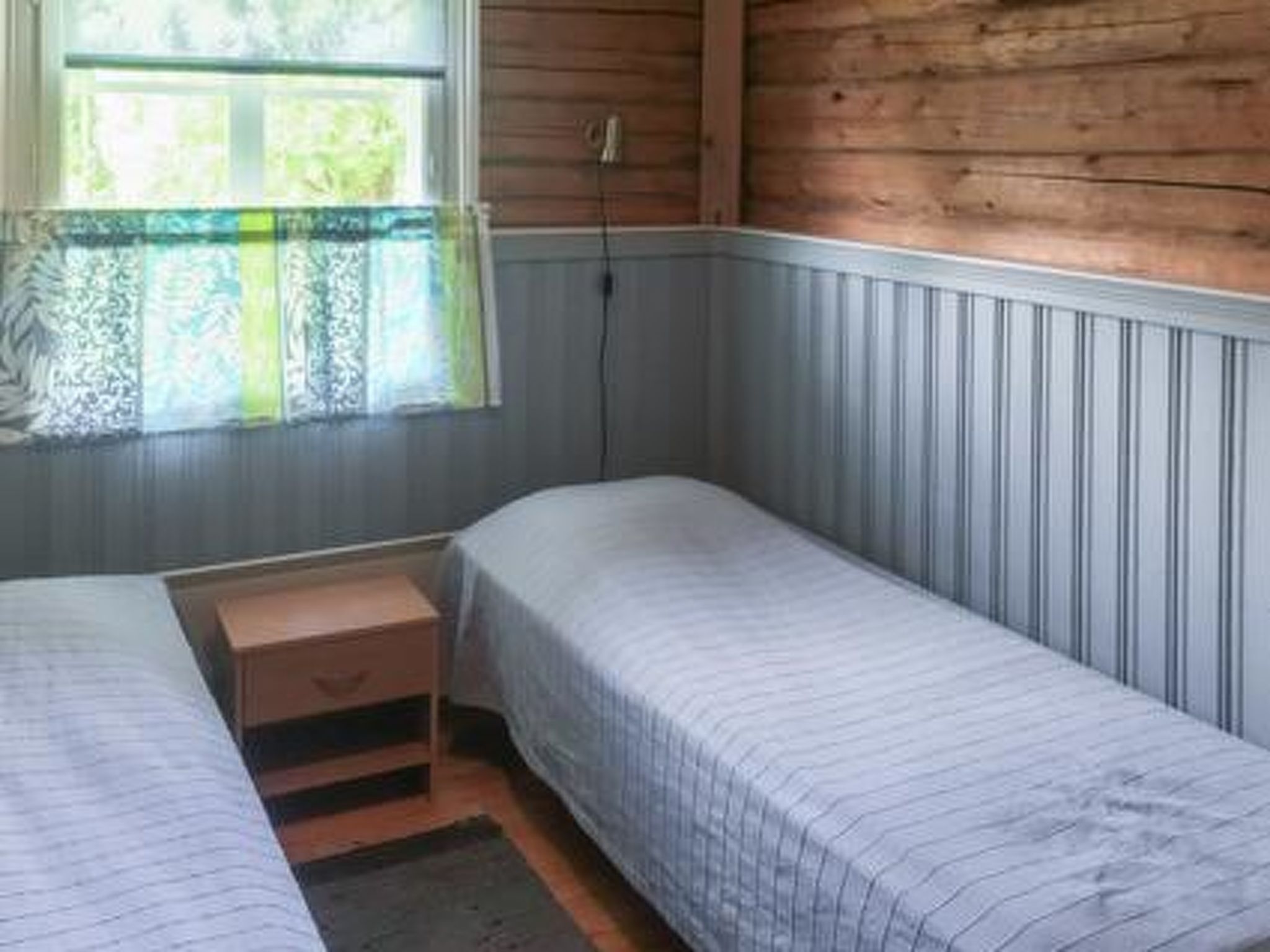Eine kleine, einräumige Holzhütte mit zwei Betten, einer Holzwand und einem Fenster mit Vorhang.