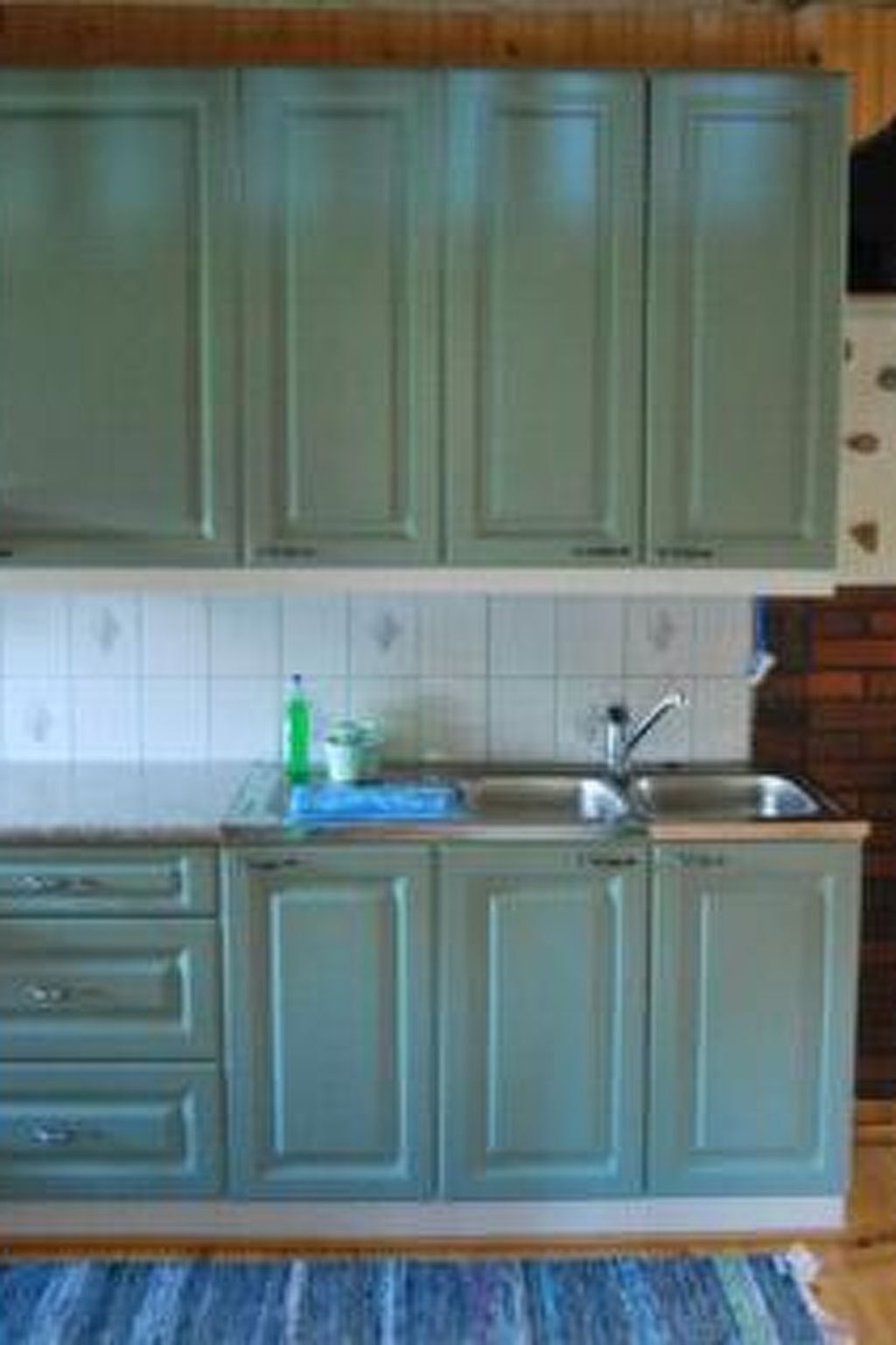 A kitchen with light green cabinets, a white tiled backsplash, and a stainless steel sink.