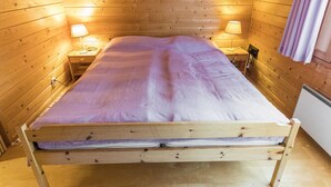 A wooden cabin room with a bed, two bedside lamps, and a window with curtains.