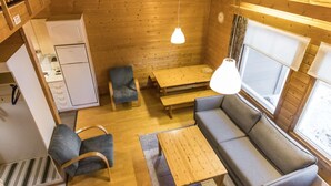 A cozy cabin interior with a wooden interior, a sofa, a dining table, a kitchen area, and a window providing natural light.