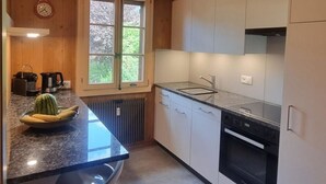 Cozinha moderna com teto de madeira, armários brancos, bancada de granito, pia e janela com vista para árvores.