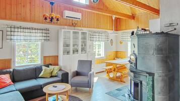 L’intérieur chaleureux d’un chalet avec un canapé, un fauteuil, une table à manger et un poêle à bois.