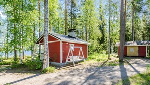 A small red cabin with a white swing set in a forested area near a body of water. - Uniranta by Interhome (Juuka)
