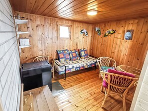 A wooden cabin interior with a sofa, two wicker chairs, a small table, and a black heater.