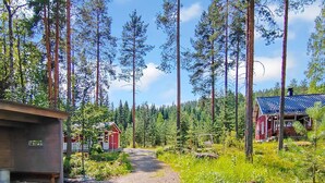 A forested area with a gravel path leading to a red cabin and a larger building with a blue roof. - Uniranta by Interhome (Juuka)