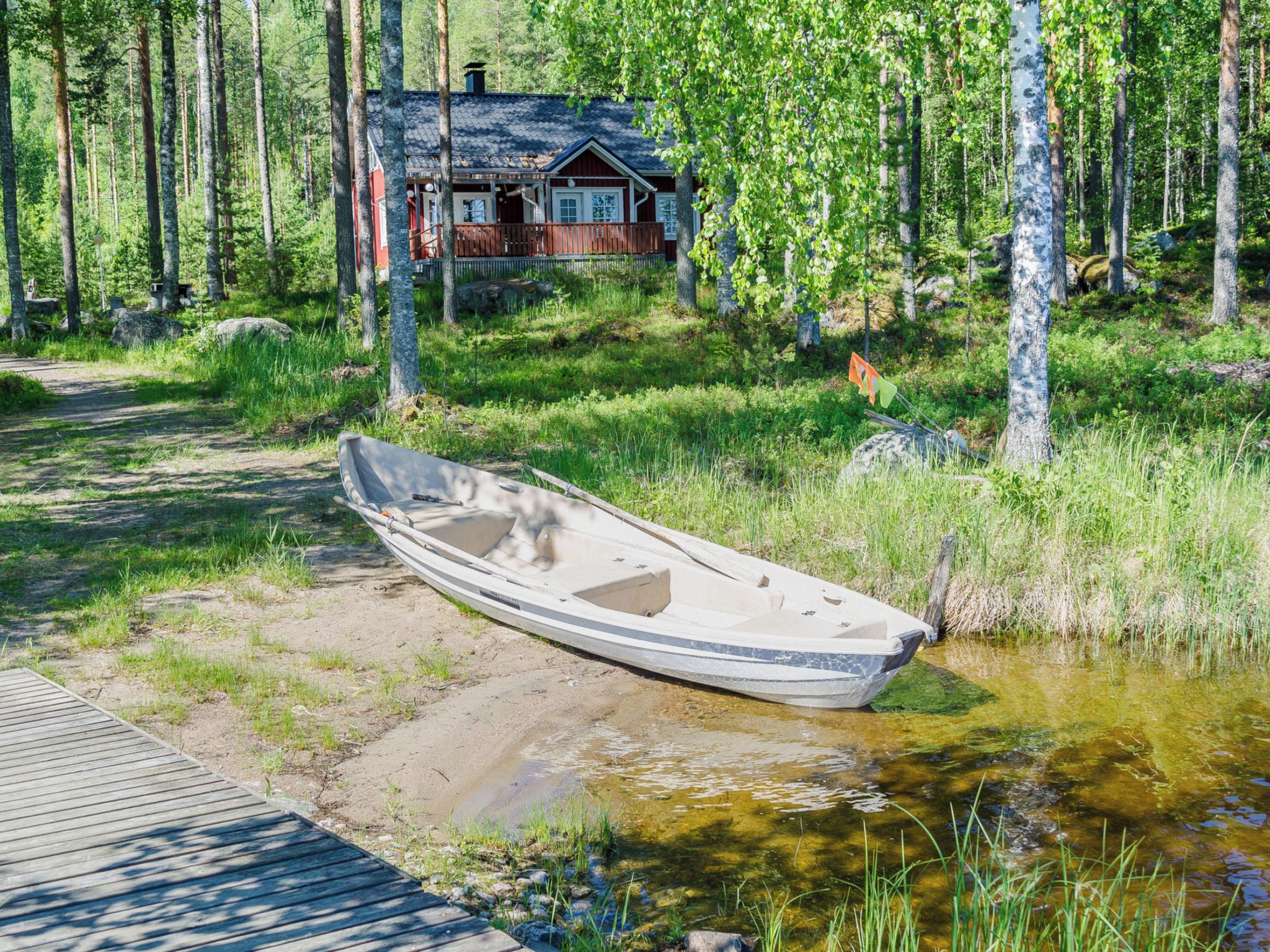 A wooden boat on a sandy shore with a house in the background surrounded by trees.