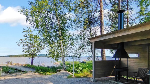 A covered outdoor area with a grill and seating, overlooking a lake. - Uniranta by Interhome (Juuka)