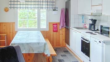 A kitchen with a wooden table, a stove, a sink, and a window with a view of greenery.