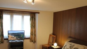Een slaapkamer met een bed, een televisie op een standaard, een houten stoel en een nachtkastje met een lamp.