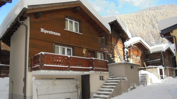 Een houten chalet met een balkon en een trap die naar de ingang leidt, omringd door sneeuw.