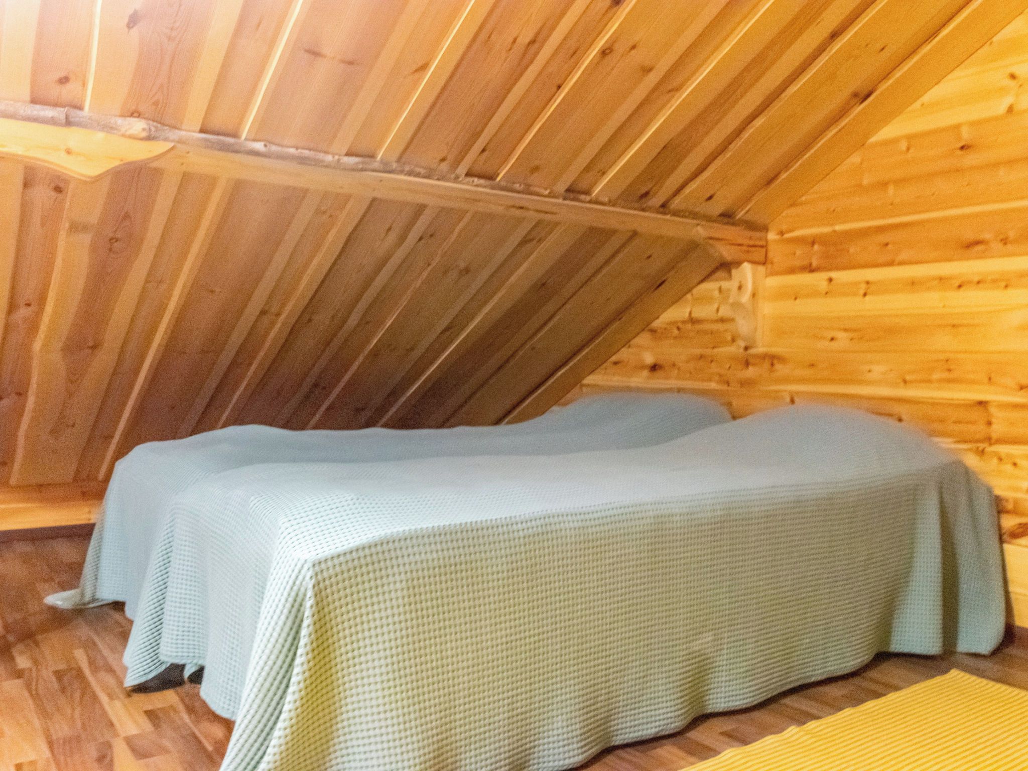 A wooden interior with a sloped ceiling and two beds with white bedding.