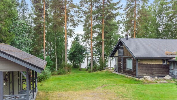 A cabin with a porch and a small deck, surrounded by a grassy yard and tall trees. - Runoniekka by Interhome (Rautalampi)