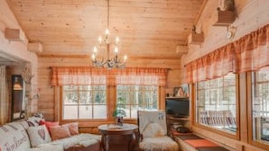 A cozy cabin interior with a wooden ceiling, a sofa with cushions, a chair, a small table, and a television.