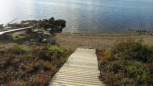 A wooden boardwalk leading to a rocky shoreline by a calm lake.