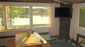 Une pièce avec une table en bois, un téléviseur fixé au mur et de grandes fenêtres avec des rideaux.