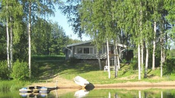 Un chalet au bord du lac, doté d’un quai, entouré de grands arbres et d’une zone herbeuse.