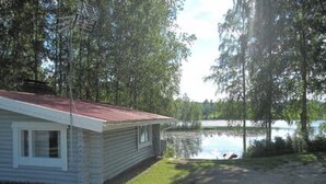 Une petite cabane avec un toit rouge, située à côté d’un lac entouré d’arbres.