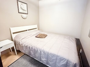 A neatly made bed with a white headboard, a small bedside table, and a framed picture on the wall.