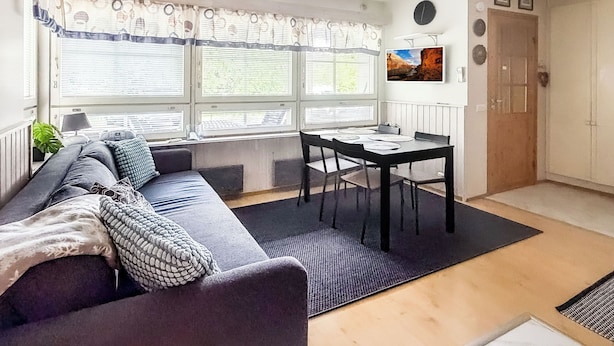 Ein Wohnzimmer mit einer Couch, einem Esstisch mit Stühlen, einem Fenster mit Jalousien, einer Heizung und einer Tür.