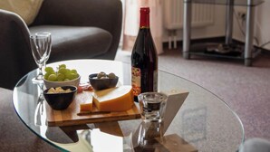 Een glazen tafel met een fles wijn, een schaal druiven, een schaal noten, een stukje kaas en een shotglas.