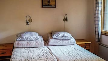 Una habitación con dos camas, cada una con un almohadón y cabecera. Hay un cuadro en la pared sobre las camas.