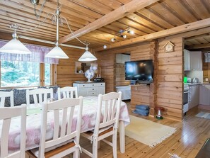 A wooden cabin interior with a dining area, kitchen, and a television.