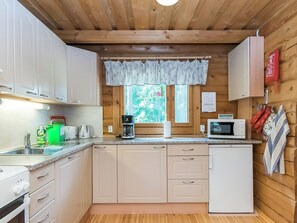 A compact kitchen with wooden cabinets, a microwave, a coffee maker, and a window with a view of greenery.