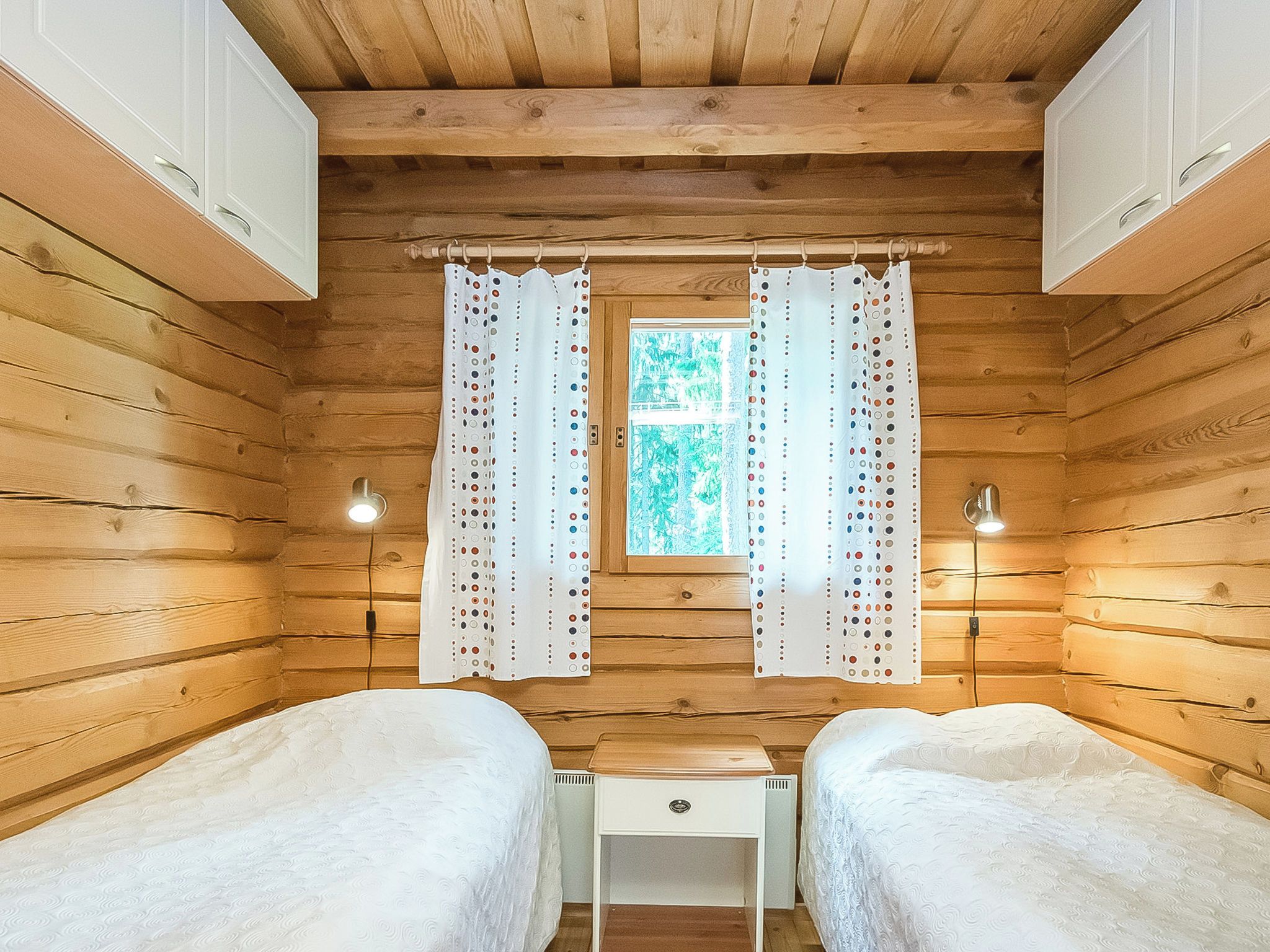 A cabin room with two beds, a small desk, and a window with curtains.