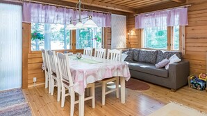Een gezellig interieur van een chalet met een eettafel, stoelen, een bank en grote ramen met uitzicht op de omgeving.
