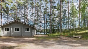 Een chalet met een grindpad, omringd door hoge bomen en een meer.