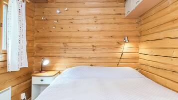 Een houten kamer met een bed, een nachtkastje met een lamp en een raam met gordijnen.
