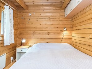 Una camera in una baita di legno, con un letto, un comodino con una lampada e una finestra con tende.