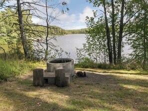A concrete fire pit with benches in a natural setting by a lake.