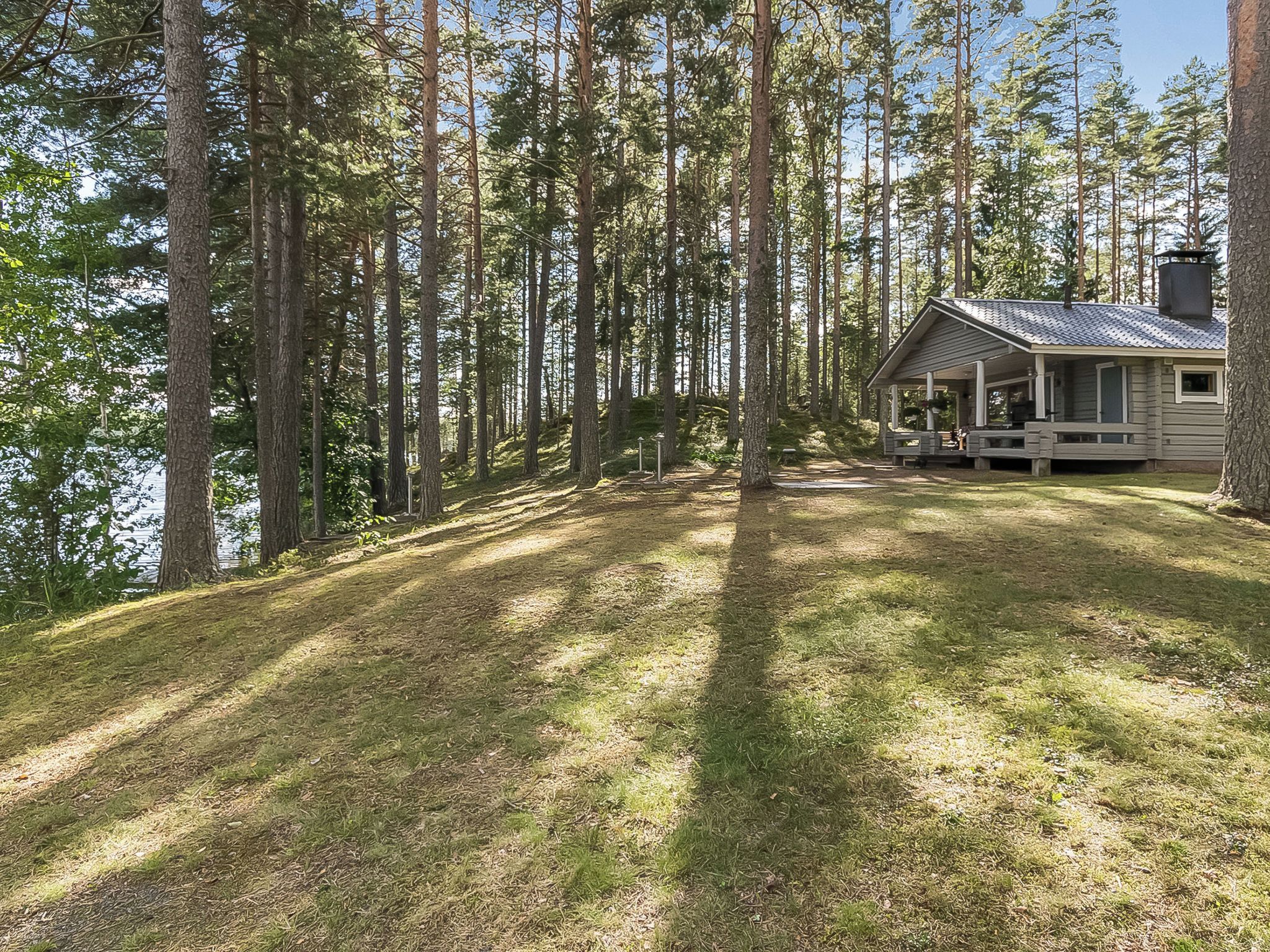 Eine Hütte mit Veranda, umgeben von hohen Bäumen und einer Rasenfläche.