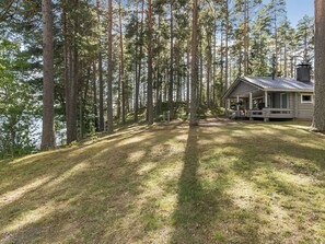 Une cabane dotée d’une véranda, entourée de grands arbres et d’une zone herbeuse.