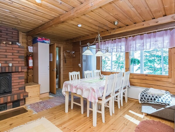 A cozy cabin interior with a dining table, chairs, a fireplace, and a window with a view of trees.