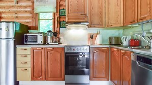 A compact kitchen with wooden cabinets, a refrigerator, a microwave, a coffee maker, and a dishwasher. - Petäjäniemi by Interhome (Kinnula)