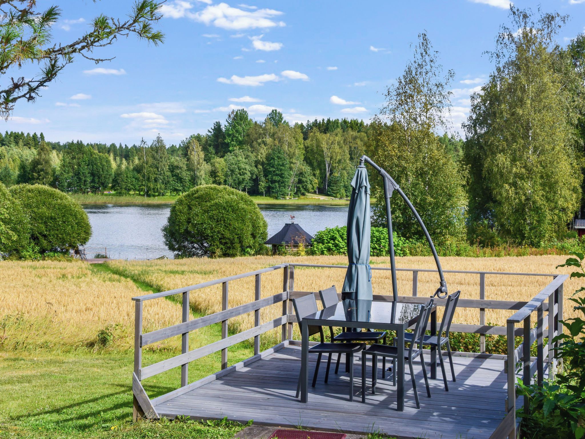 A wooden deck with a table and chairs, overlooking a lake and forest.