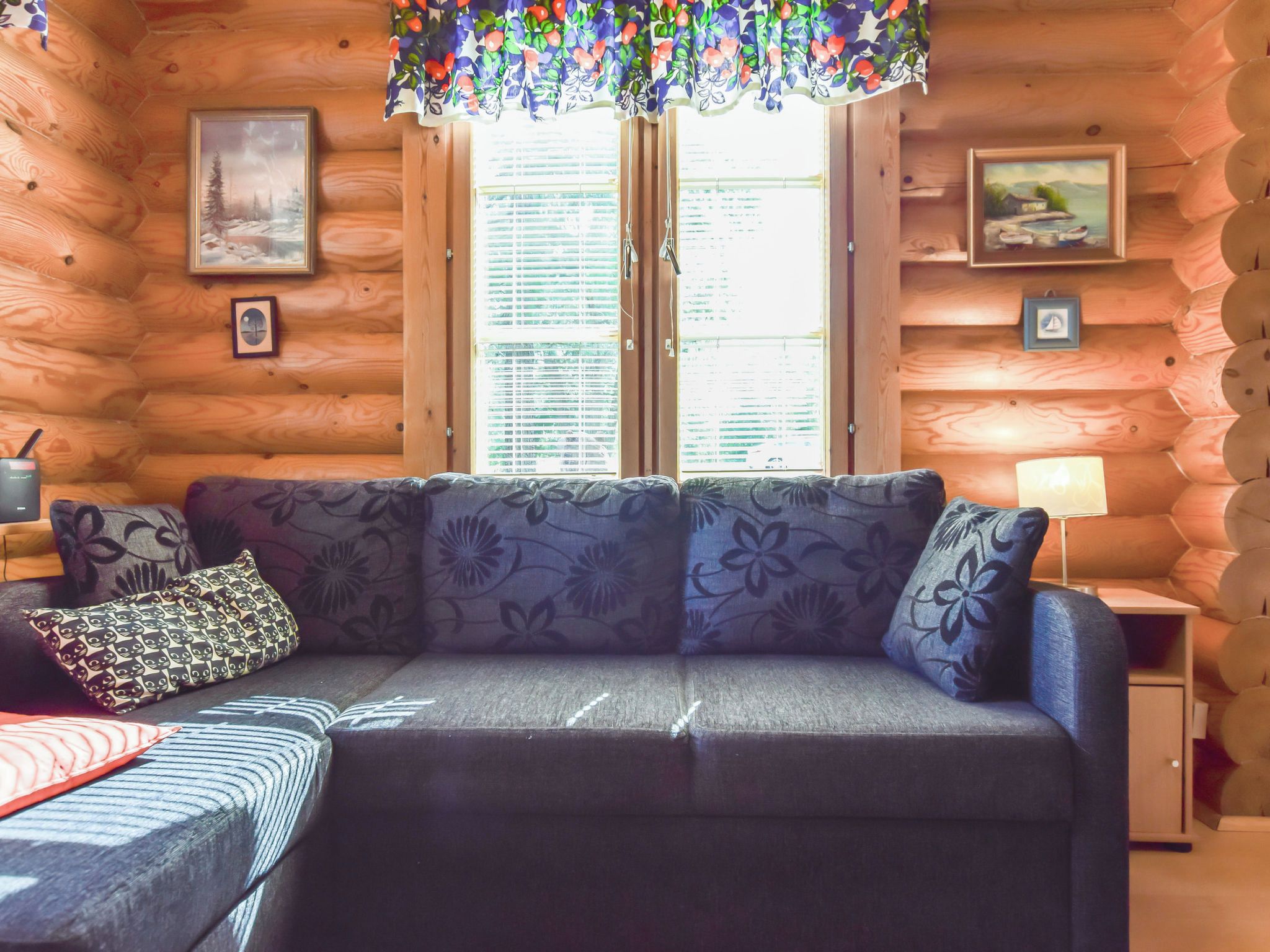 A cozy cabin interior with a sofa, pillows, a lamp, and framed pictures on the walls.
