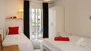 Ett hotellrum med två sängar, ett skrivbord, en stol, en lampa och en skjutdörr i glas som leder ut till ett utomhusområde.