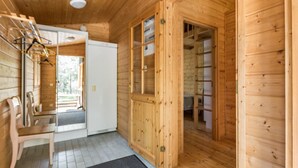 Interior em madeira com porta para uma varanda, área de estar com cadeiras e uma estante embutida.
