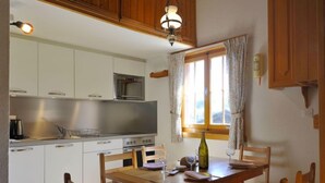 A kitchen with white cabinets, a microwave, and a wooden dining table with chairs. - Mountain View by Interhome (Moléson-sur-Gruyères)