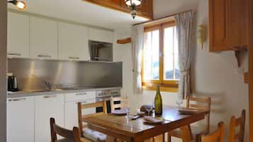 Une cuisine avec des meubles blancs, un four à micro-ondes et une table à manger en bois, accompagnée de chaises.