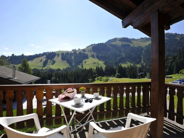 Une terrasse en bois avec une table et des chaises, offrant une vue sur un paysage montagneux.