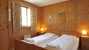 A wooden-paneled room with two beds, each with a nightstand and a lamp. - Mountain View by Interhome (Moléson-sur-Gruyères)